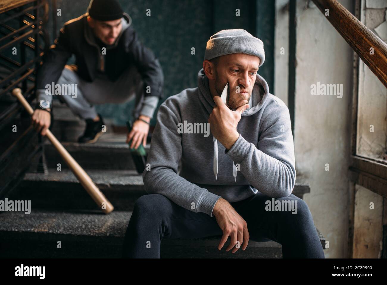 Two male hooligans are sitting on the stairs. Street robbers with baseball bat and knife waiting for victim. Crime concept Stock Photo