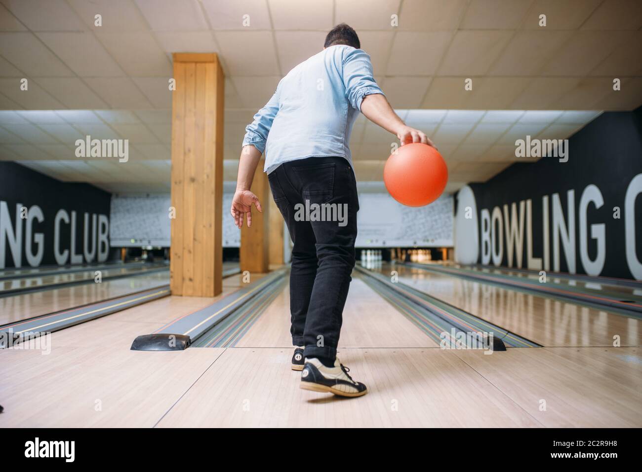 Male bowler standing on lane and poses with ball in hands, back view. Bowling alley player prepares to throw strike shot in club, active leisure Stock Photo