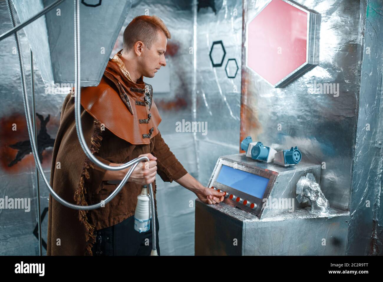 Space scientist holds wires at the control panel in spacecraft with foil walls. Fantasy spaceship for interstellar travel, future science and technolo Stock Photo
