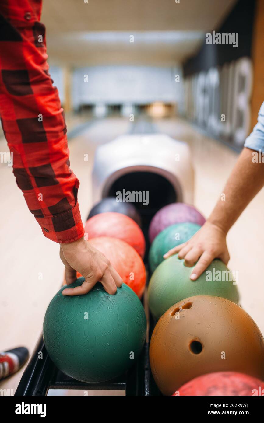 Two male bowlers takes balls from feeder. Bowling alley players