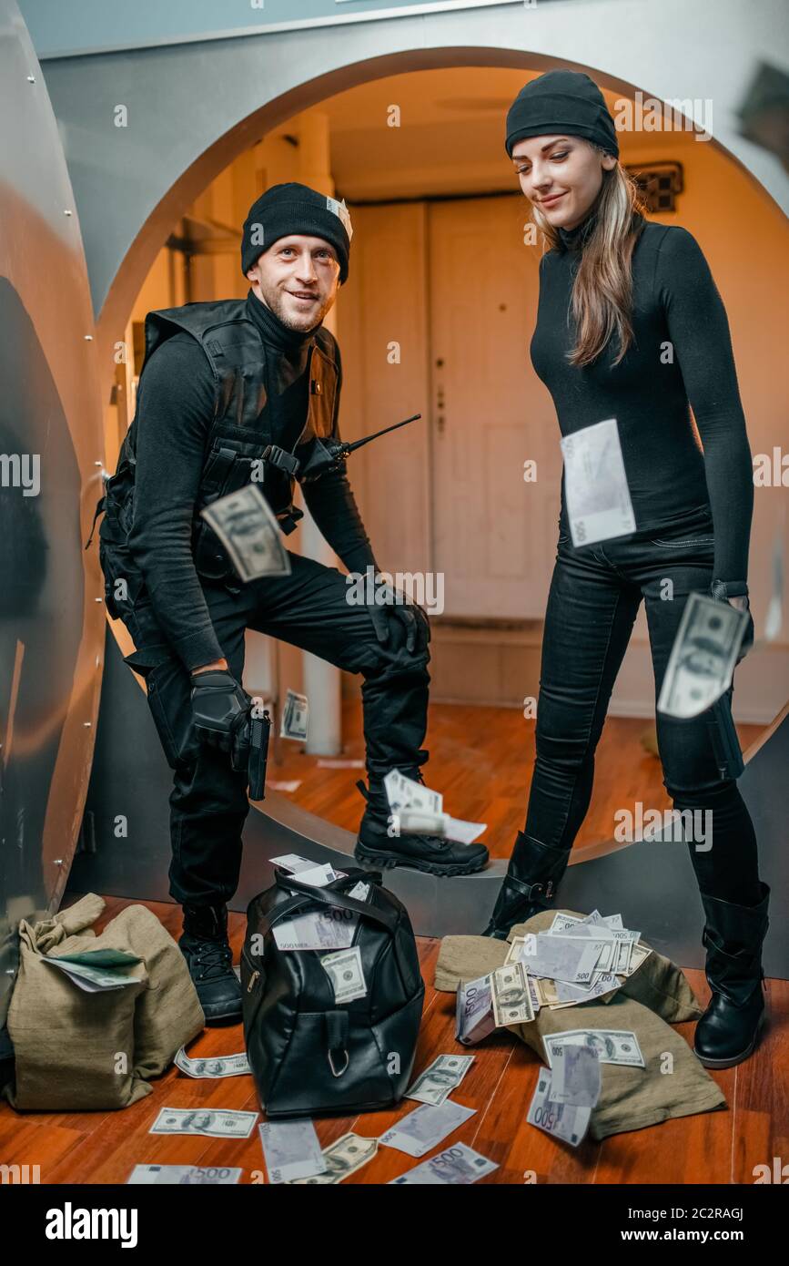 Bank robbery, two happy robbers in black uniform throwing money at the