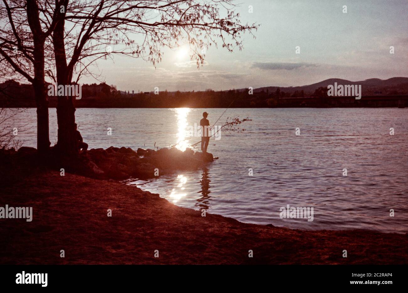 Man fishing at the water at sunset or sunrise. Shot on analog film. Stock Photo