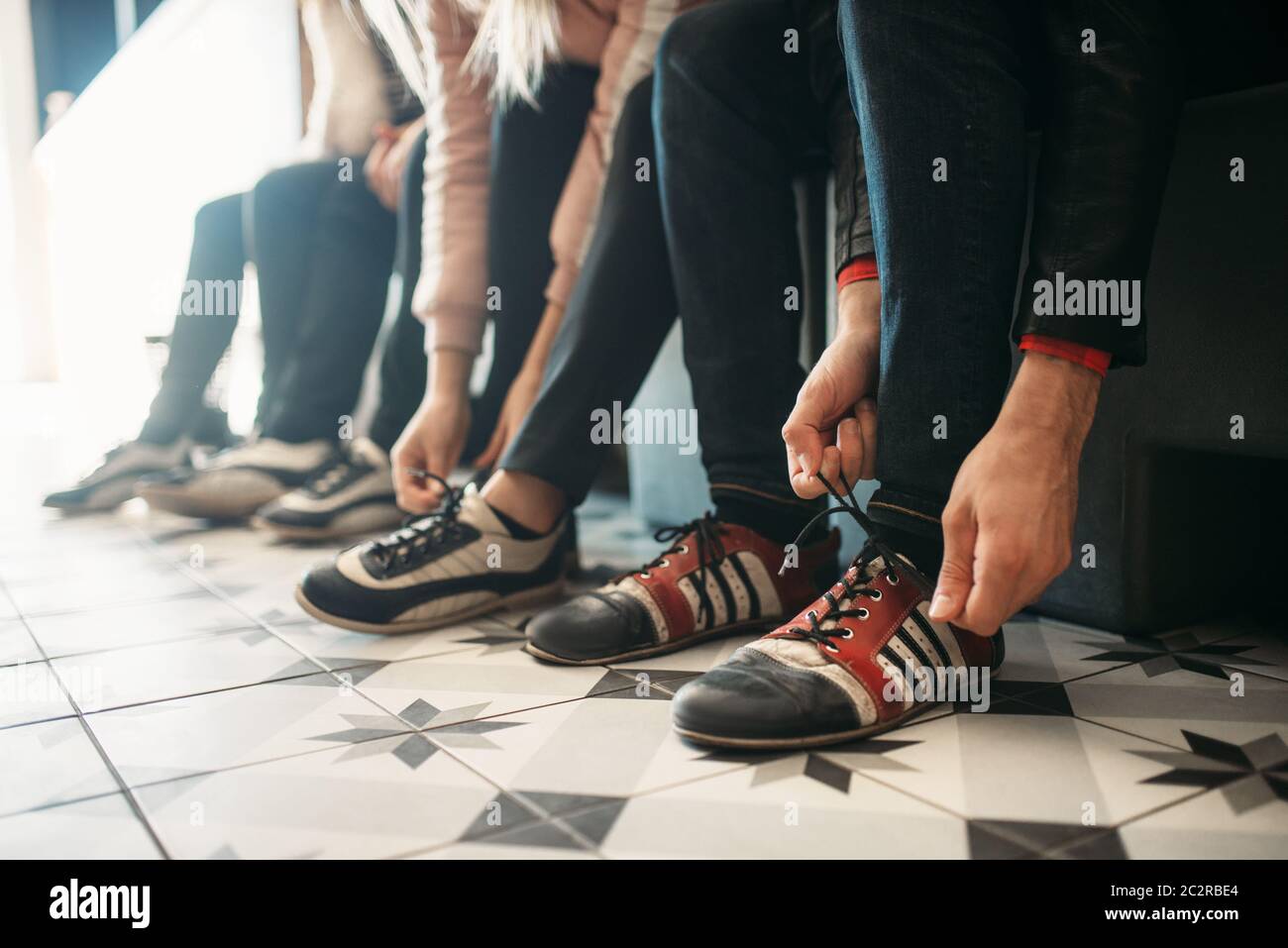 Bowling alley players ties shoelaces on house shoes. Bowlers sitting on the bench and prepares to competition in club, active sport. Bowl sport Stock Photo