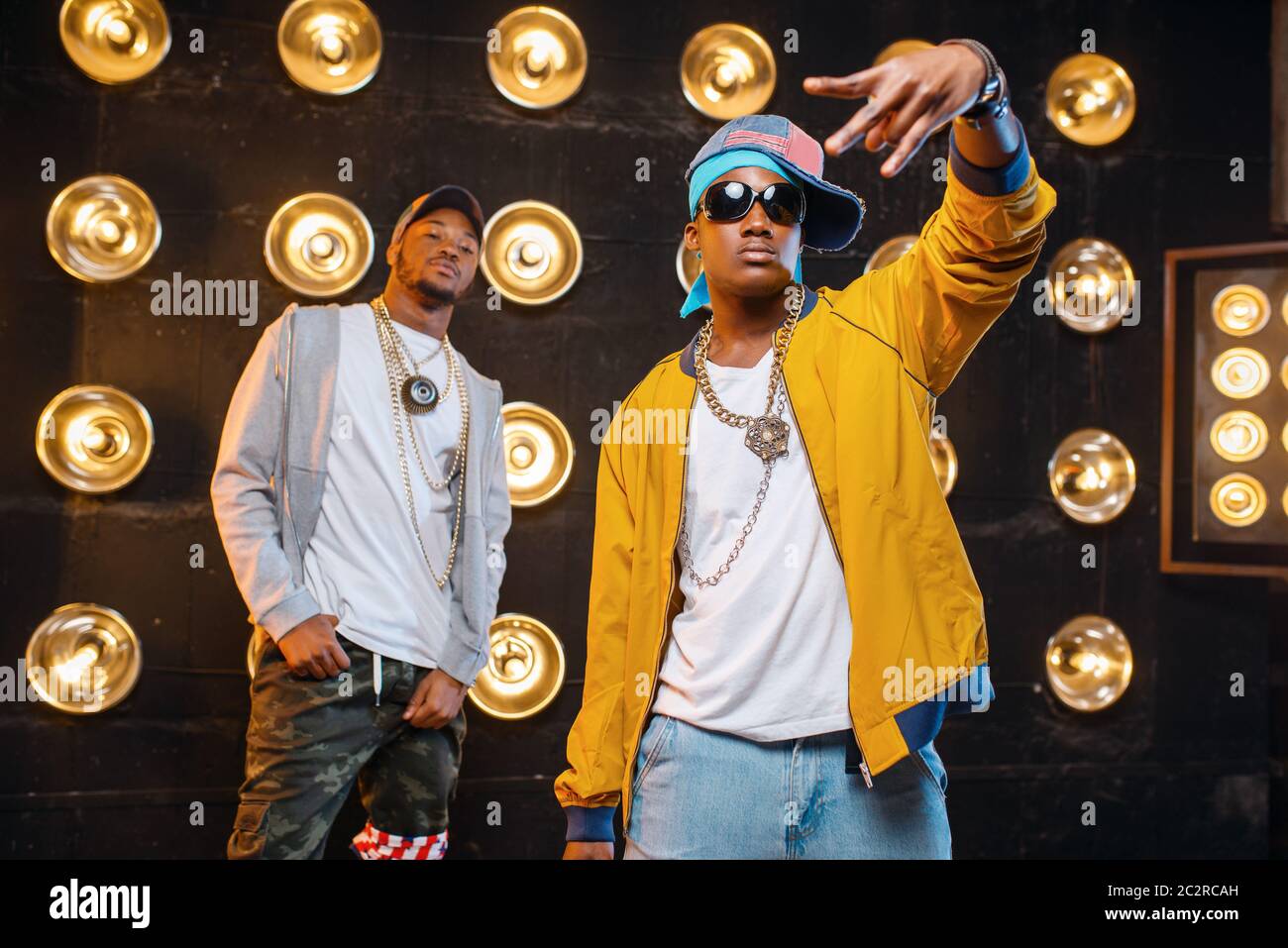 Two black rappers in caps on stage with spotlights on background. Rap performers on scene with lights, underground music, urban style Stock Photo