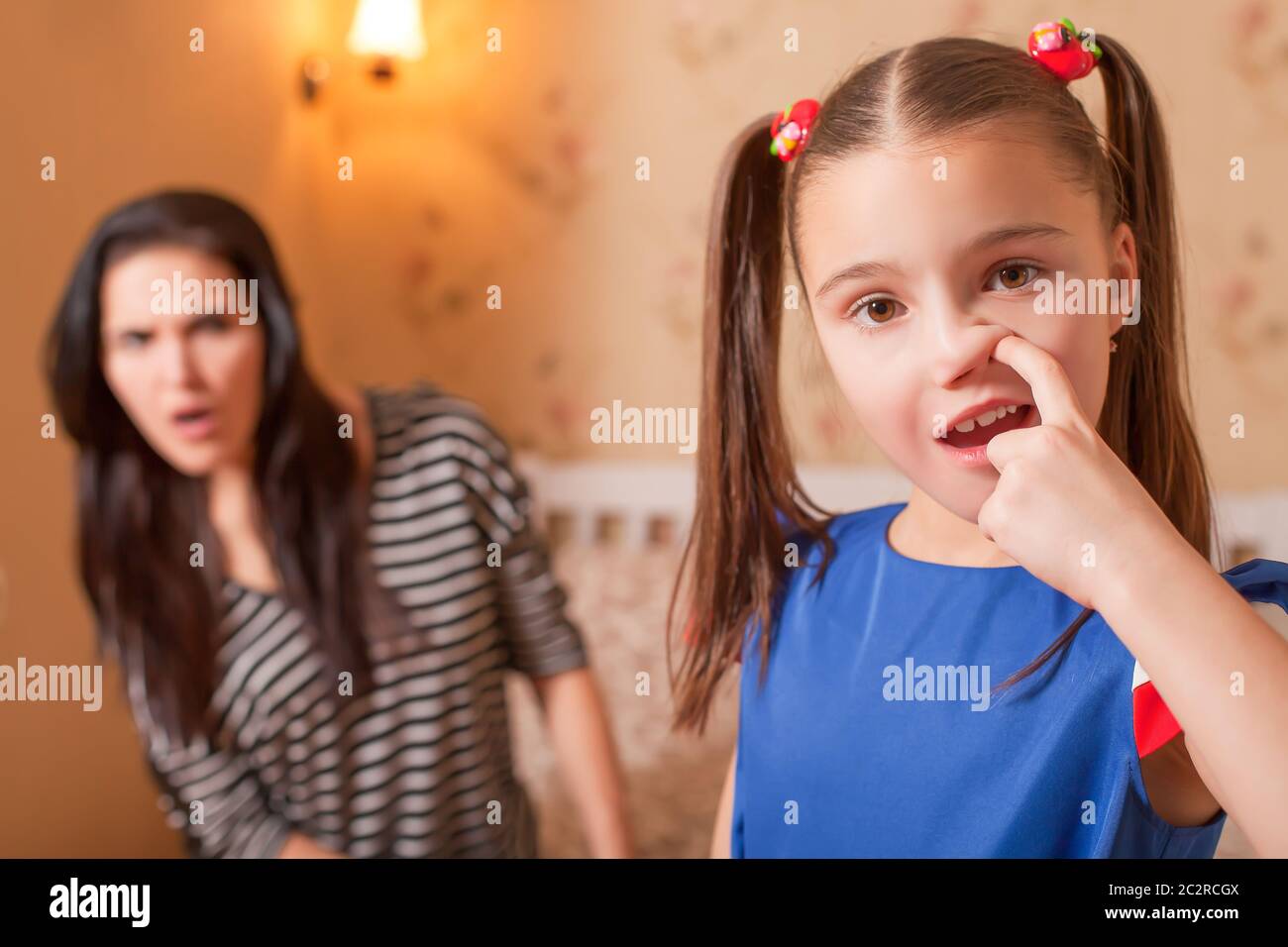 Curious girl picking a nose against surprised mother on the background. Stock Photo