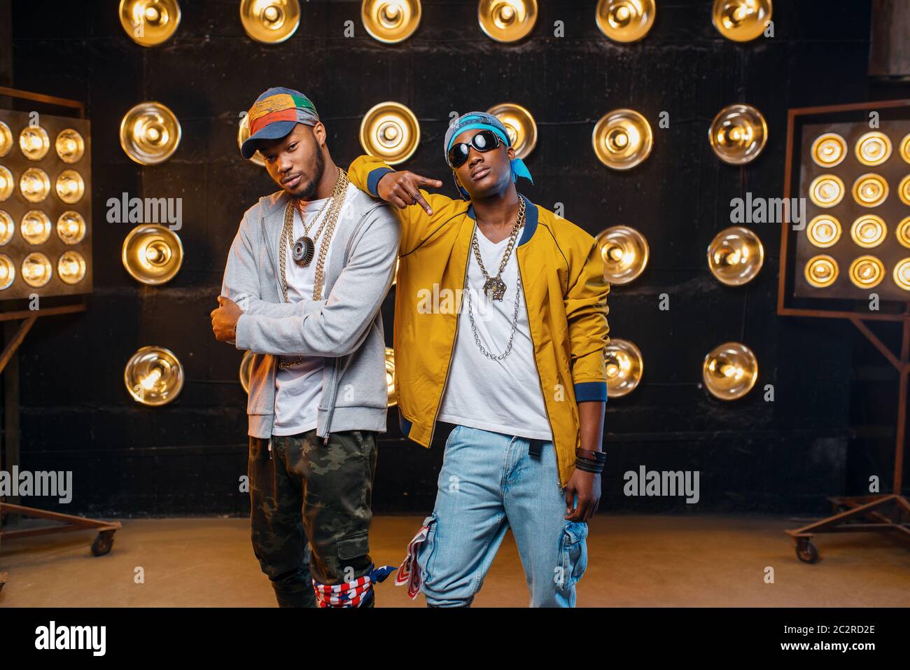 Two black rappers in caps, artists poses on stage with spotlights on background. Rap performers on scene with lights, underground music Stock Photo