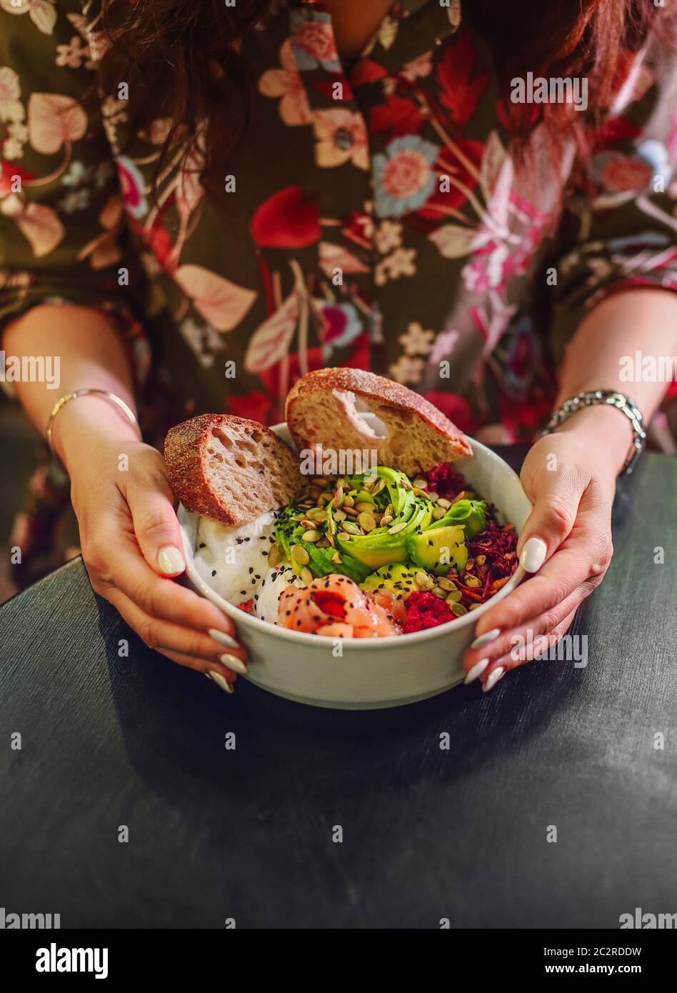 Woman eating organic food. Fresh seafood recipe. Fresh salmon poke bowl with rice, egg, bread, fresh red cabbage, avocado, radis Stock Photo