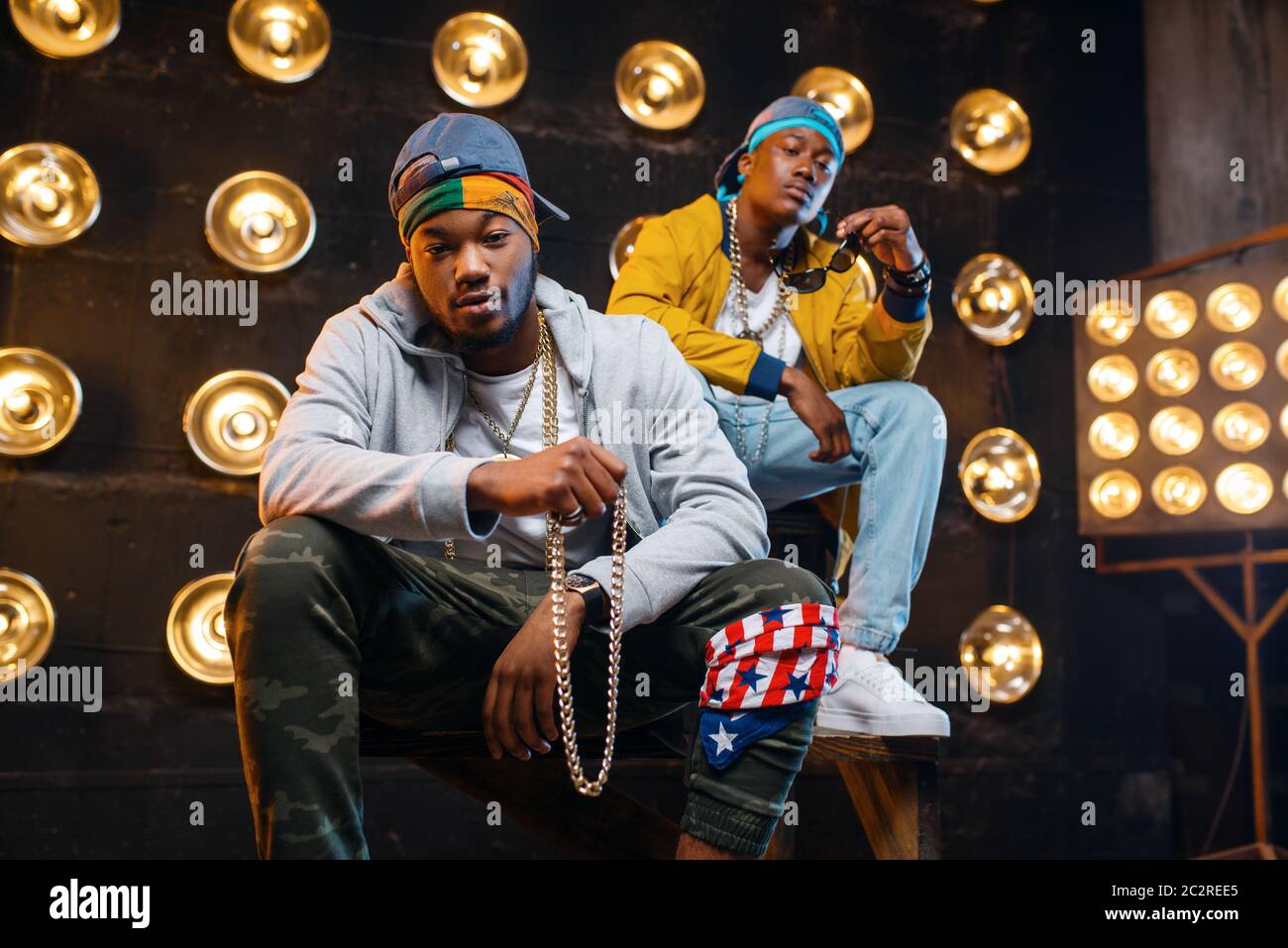 Two black rappers sitting on the steps, perfomance on stage with spotlights on background. Rap performers on scene with lights, underground music, urb Stock Photo