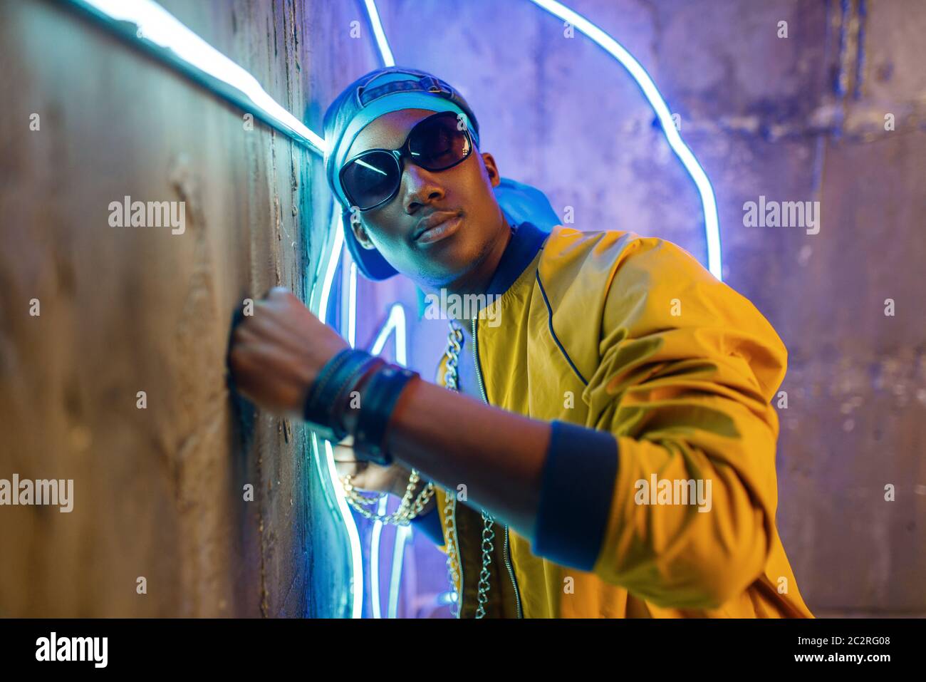 Black rapper in underpass neon light on background. Rap performer in club with grunge walls, underground music Stock Photo