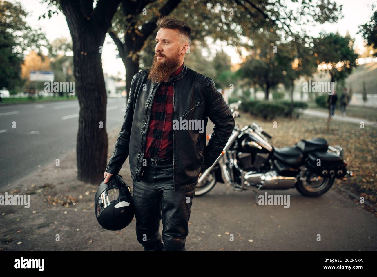 Bearded biker with helmet in hand in front of his chopper, back view. Vintage bike, road rider and his motorcycle, freedom lifestyle, biking Stock Photo