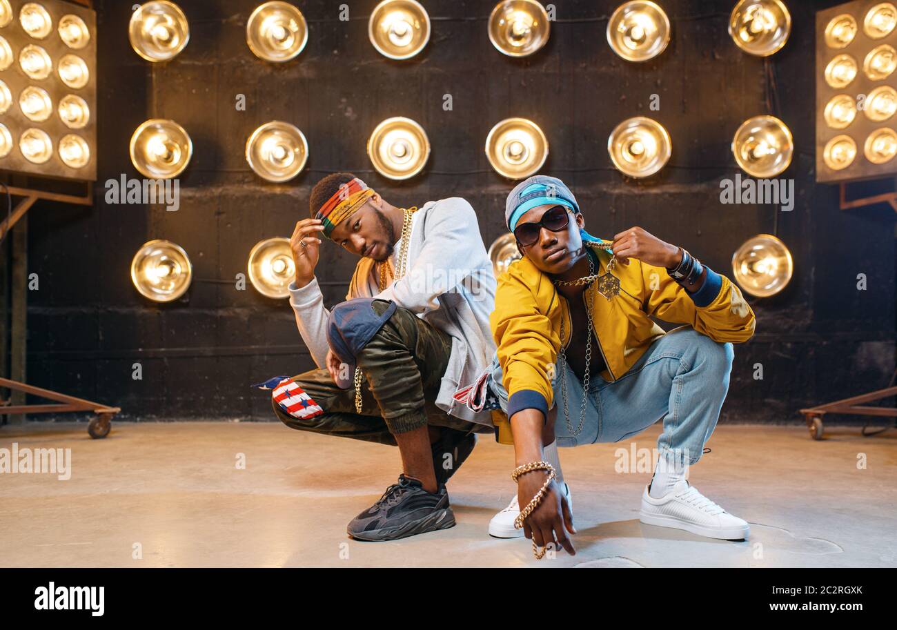 Two black rappers sitting on the floor, perfomance on stage with spotlights on background. Rap performers on scene with lights, underground music, urb Stock Photo
