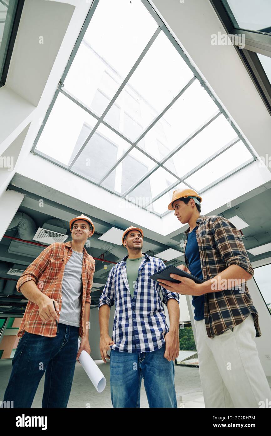 Vertical low angle view shot of joyful young construction engineers standing together talking about their work Stock Photo