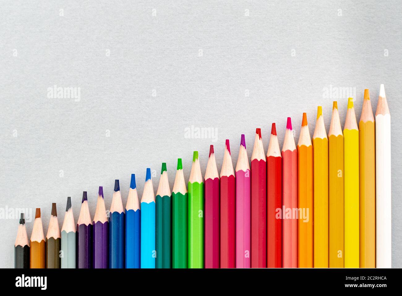 a set of colourful pencils lined up in a row getting taller from dark to light Stock Photo