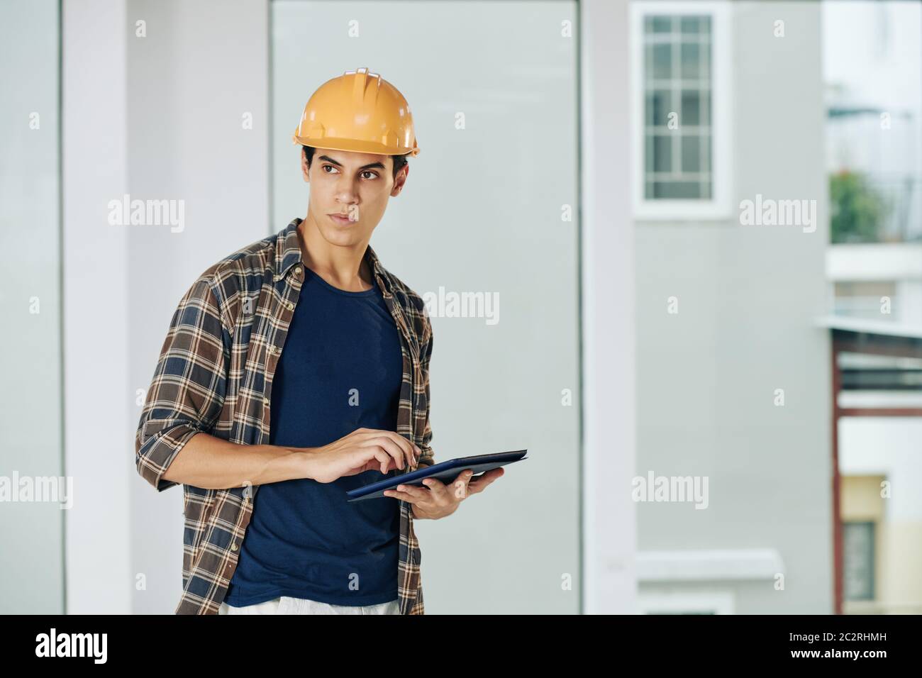 Horizontal medium shot of young engineer standing alone in empty room using tablet computer looking away, copy space Stock Photo