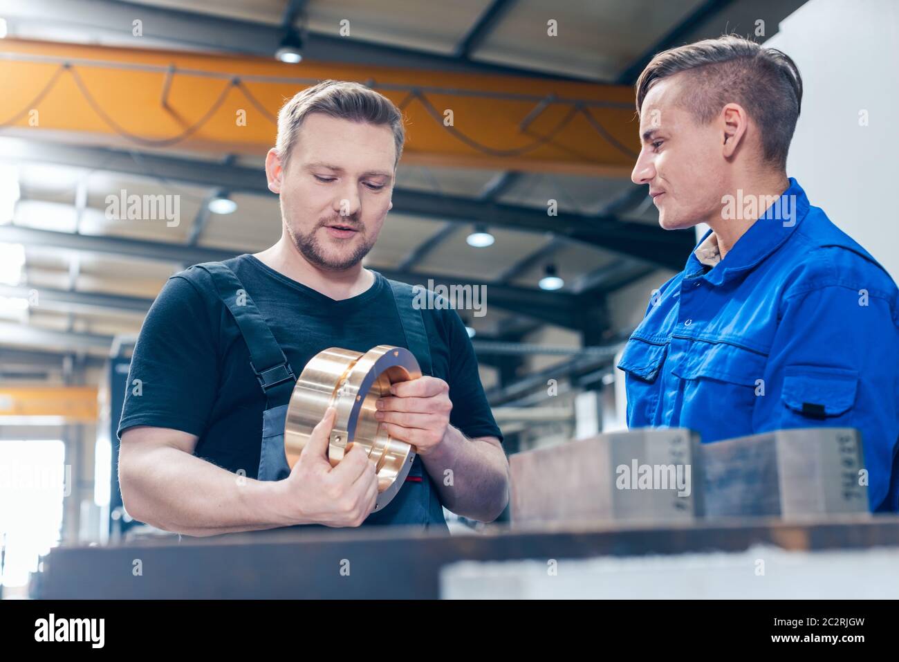 Skillful master discussing a workpiece with his apprentice or trainee Stock Photo