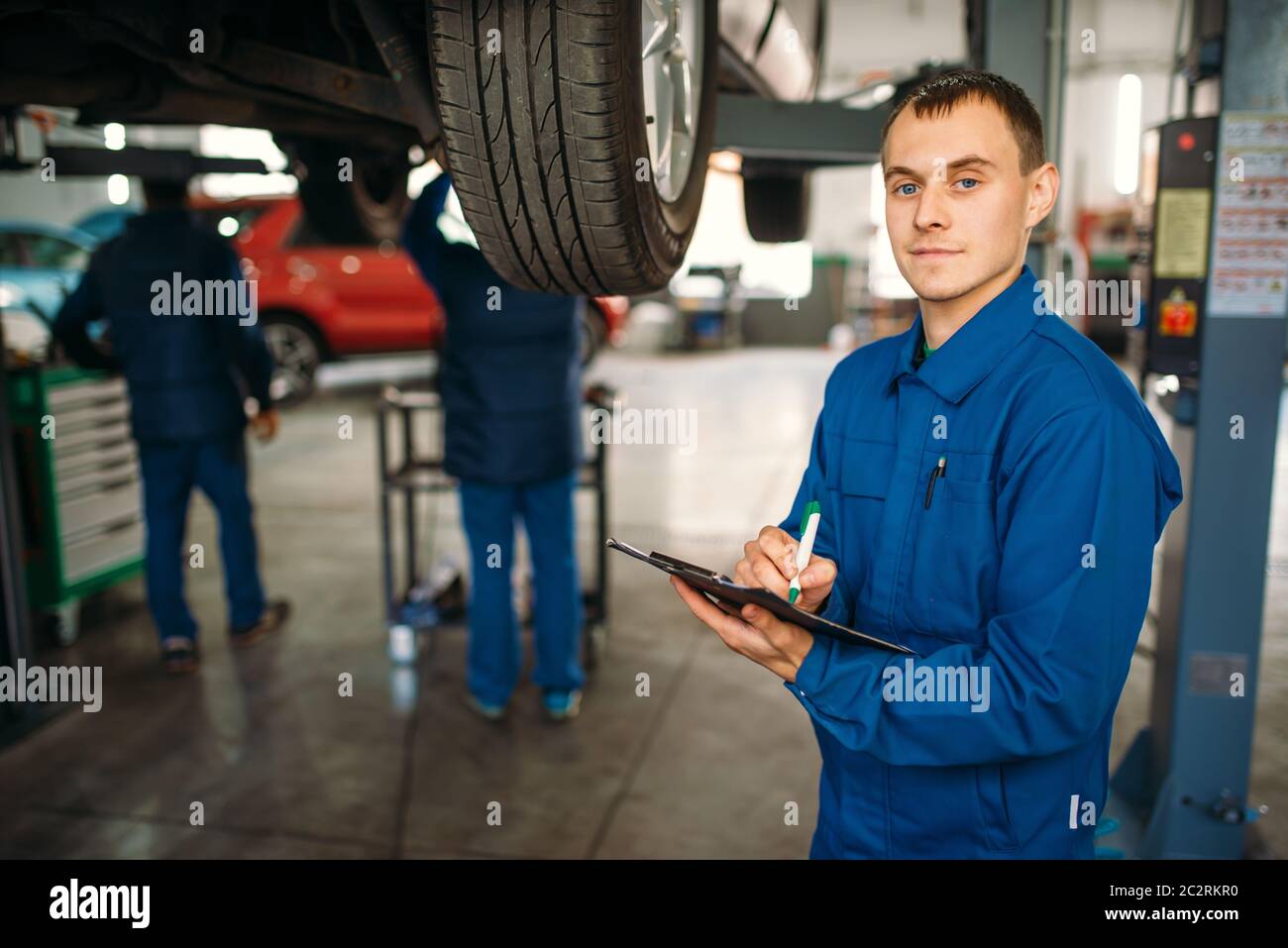 Repairman with notebook fills the check list, car on the lift, fixing
