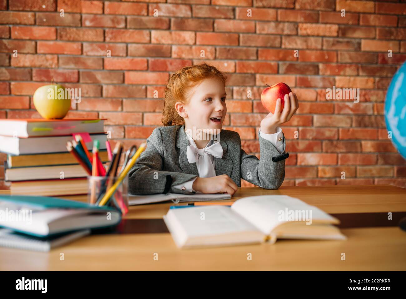 Funny schoolgirl with apple sitting at the table in classroom. Female ...