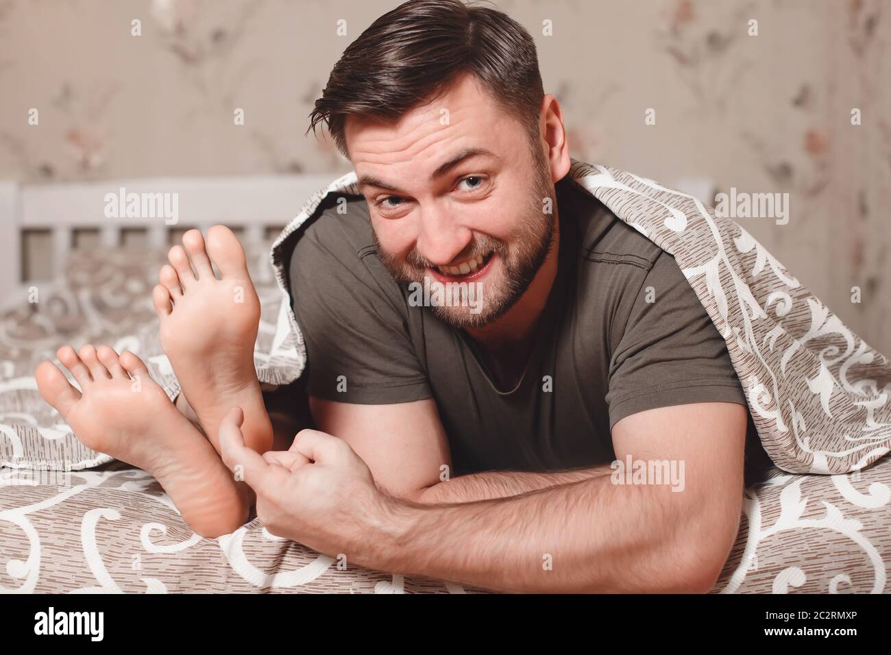 Playful man trying to tickle woman's feet in bed. Stock Photo