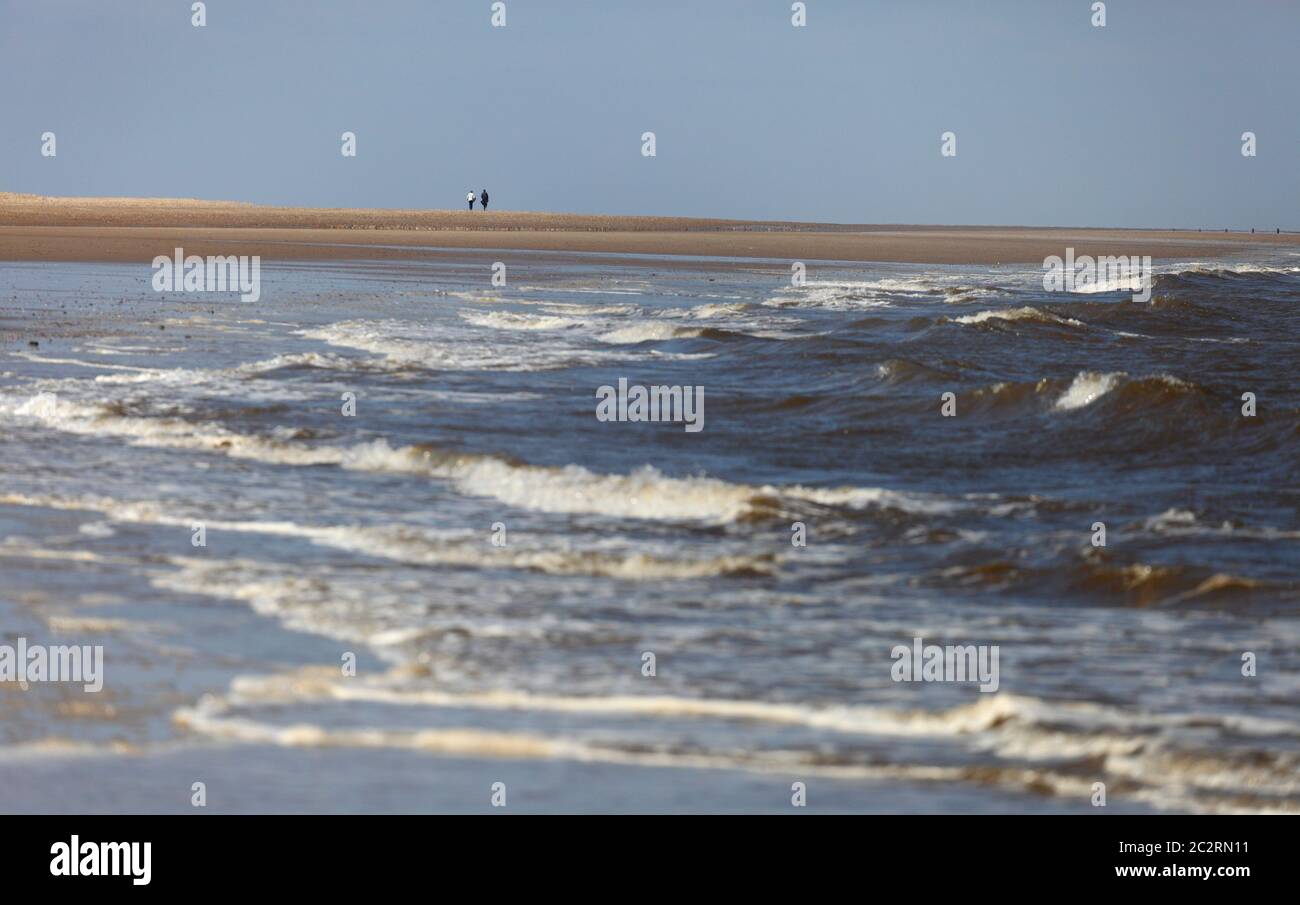 Two people walking in the distance along the beach at Thornham on the North Norfolk coast, England. Stock Photo