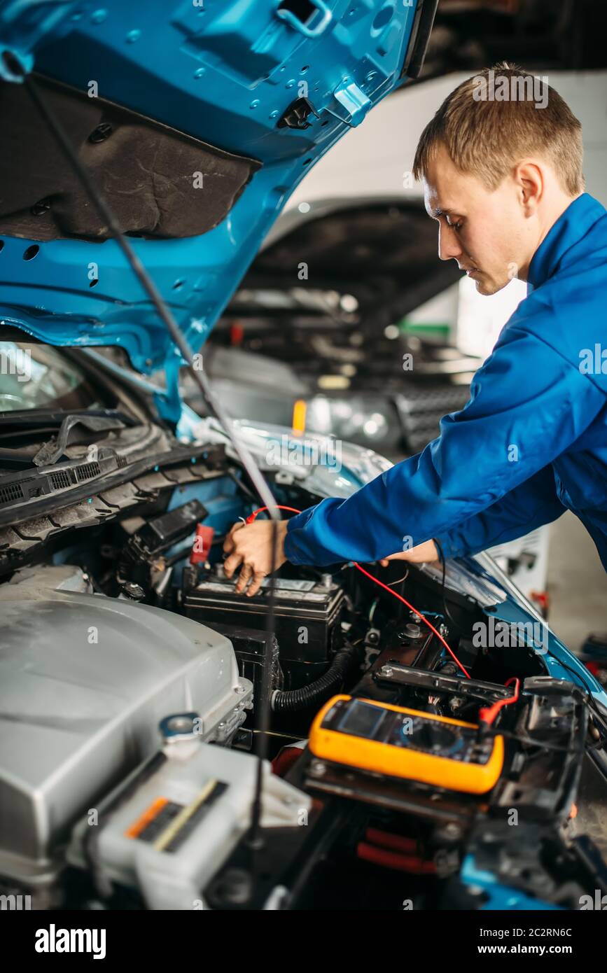 Car electrician with multimeter checks the battery level. Autoservice