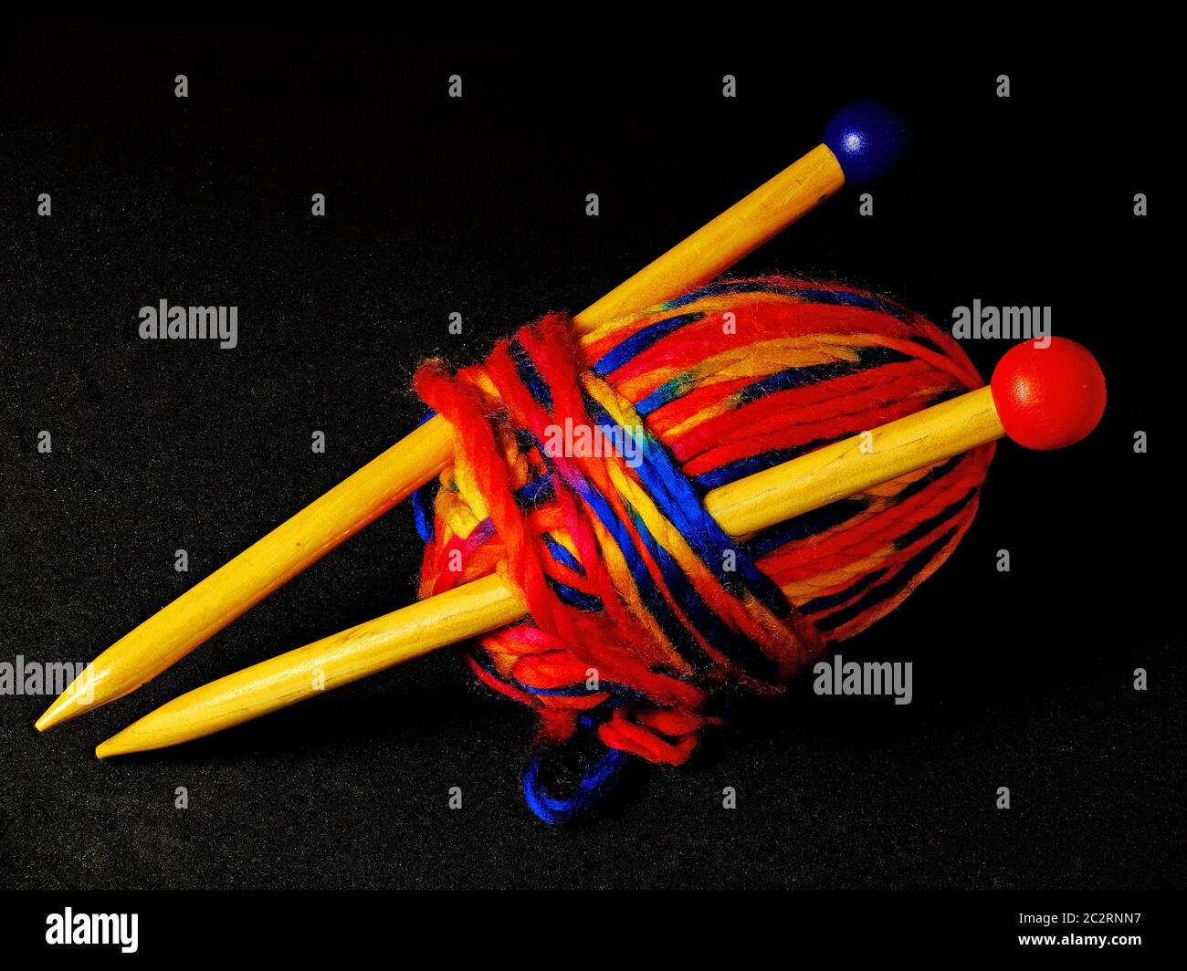 Ball of thick multi coloured wool and 2 knitting needles against black