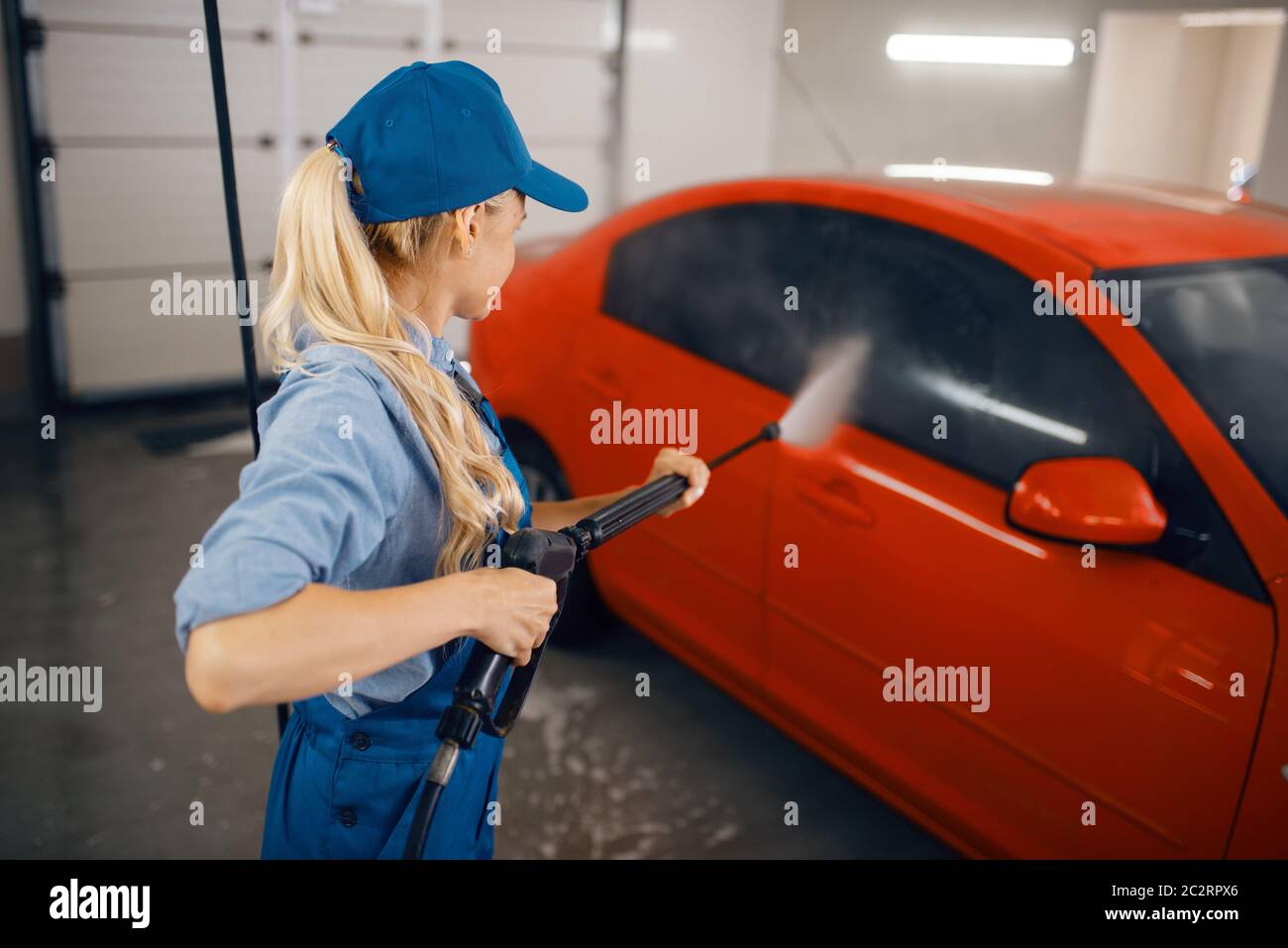 Female washer in uniform cleans the auto with high pressure gun in