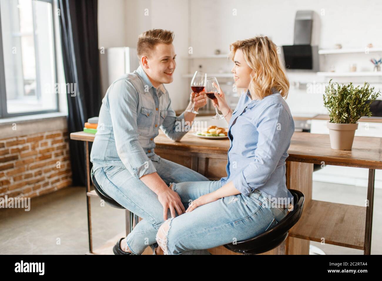 Attractive love couple sitting at the table, romantic dinner. Man and woman drinks wine and eats fruits on the kitchen. Happy lifestyle, beautiful rel Stock Photo