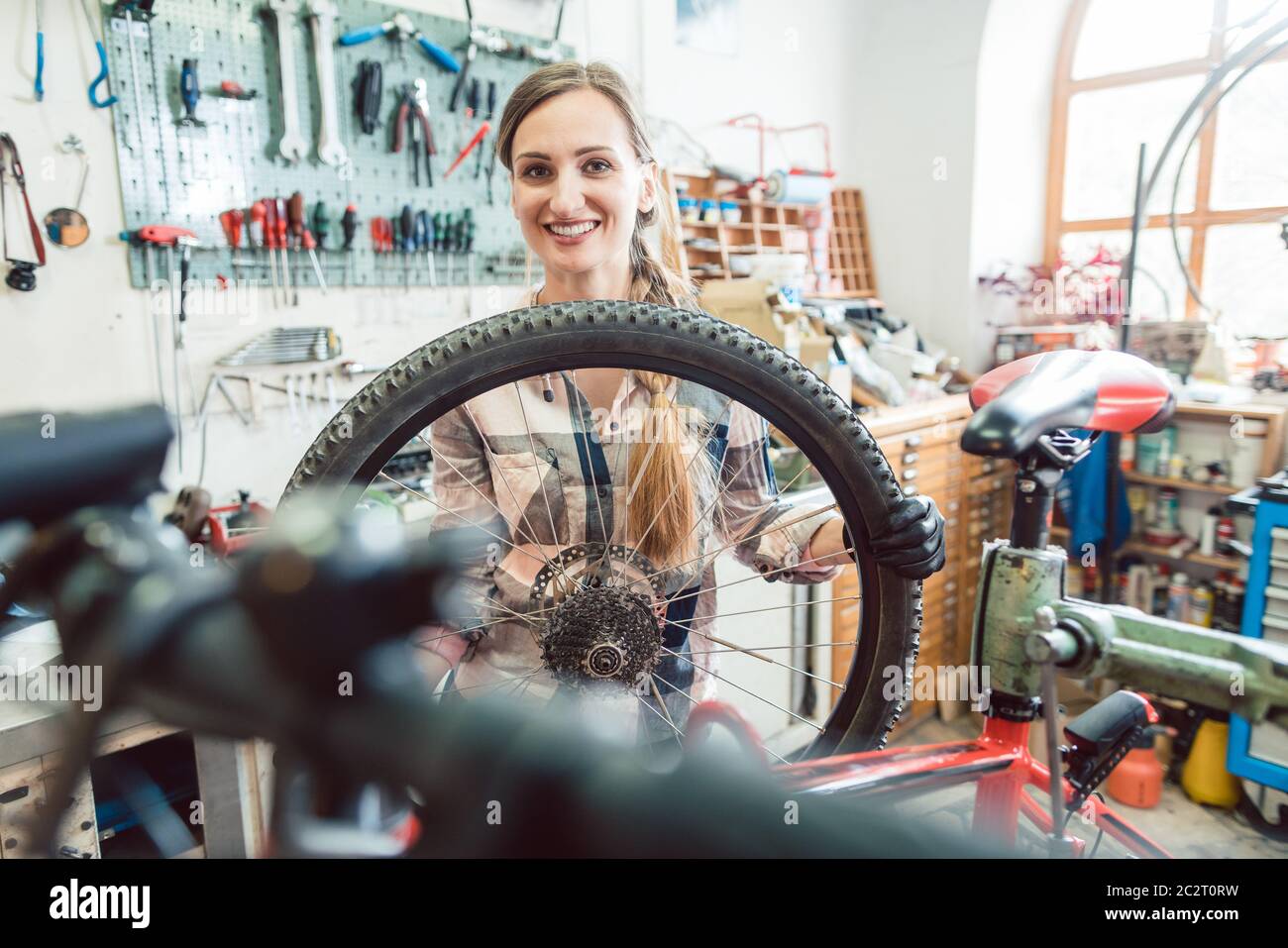 Very happy bike mechanic woman looking through the wheel of bicycle Stock Photo