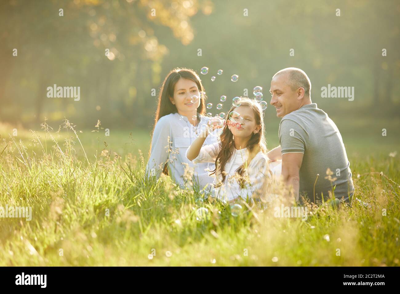happy family with child girl blow soap bubbles outdoor in sunny summer ...