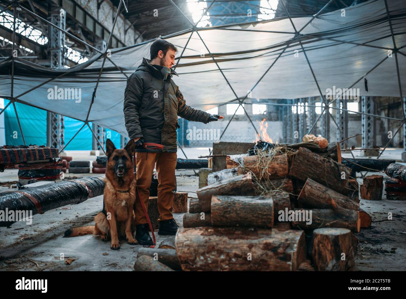 Stalker with his domestic animal against fireplace, man lives in a post apocalyptic world. Post-apocalypse lifestyle on ruins, doomsday, judgment day Stock Photo