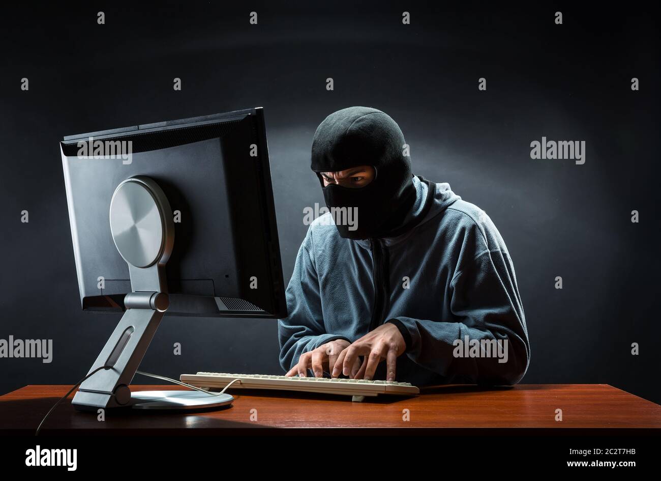 Hacker in balaclava mask stealing information in the office Stock Photo