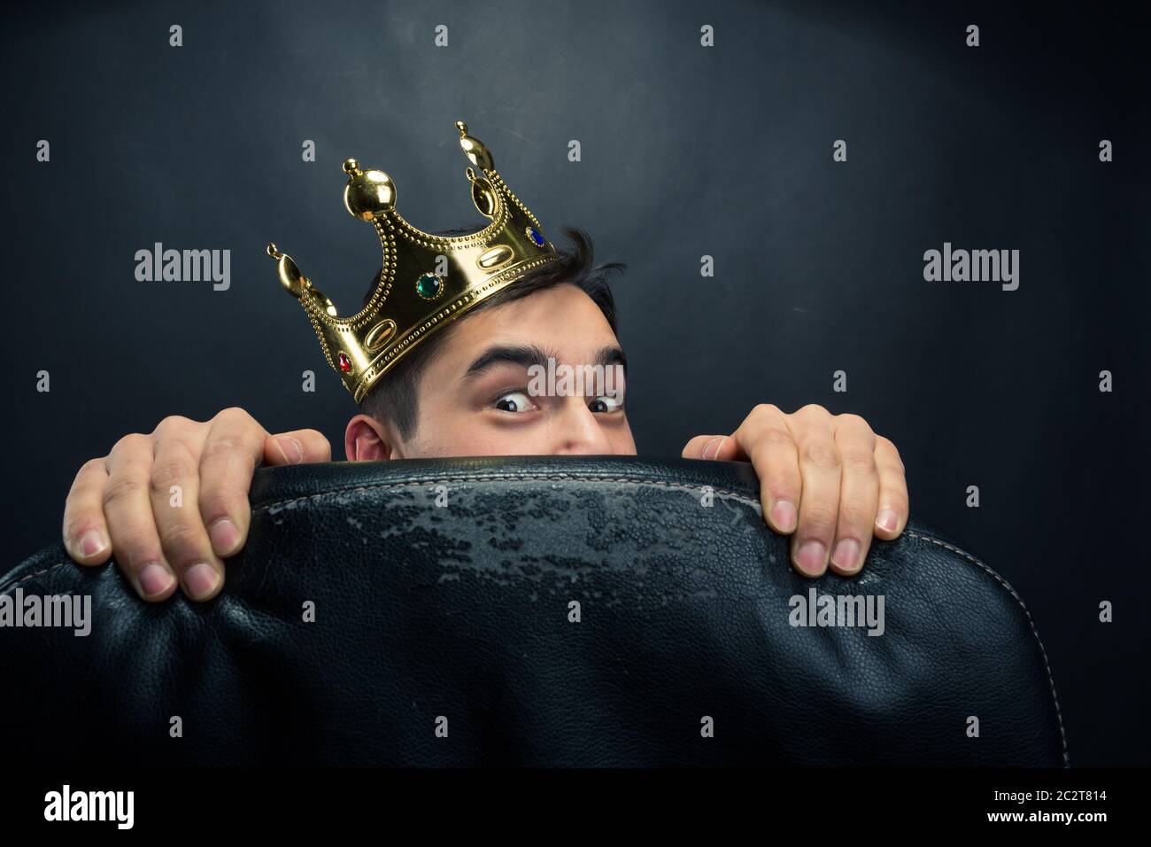 Scared man with crown on the head hidding behind the chair Stock Photo