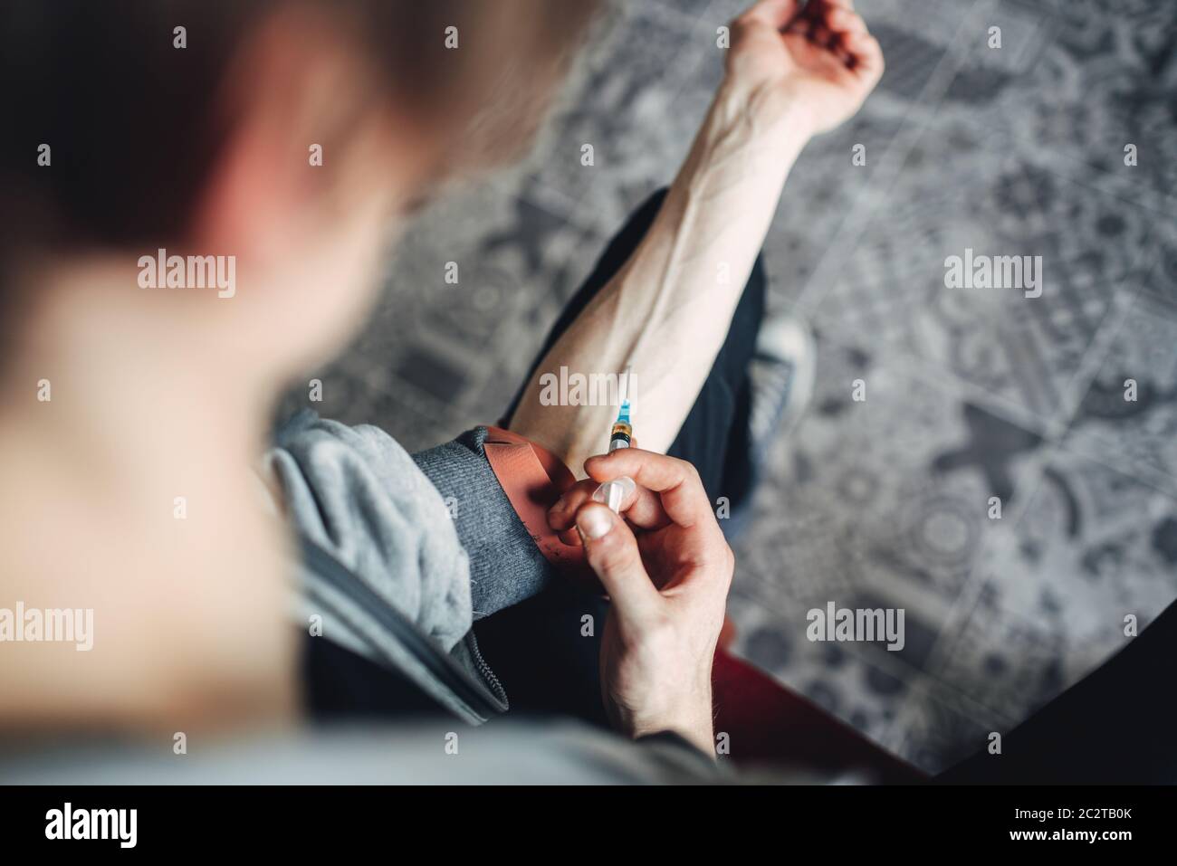 Male junky with a syringe doing an injection dose in the arm. Narcotic addiction concept, drug addicted people Stock Photo