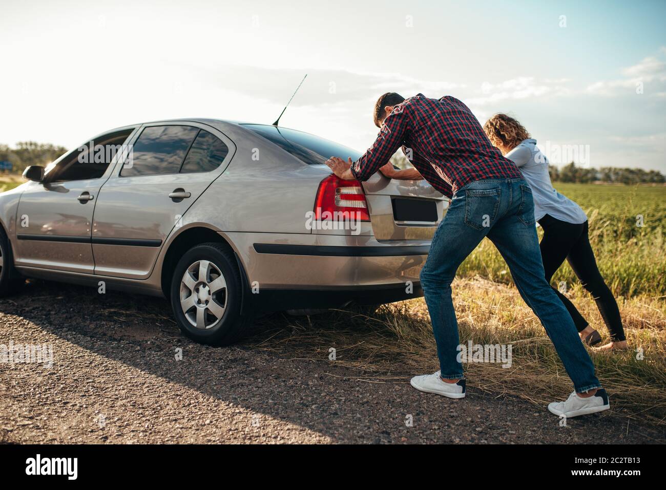 Man and woman pushing a broken car down the road, back view. Vehicle