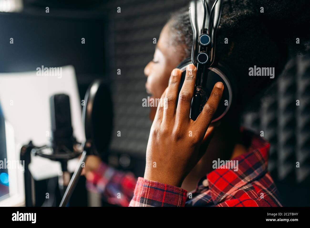 Young woman in headphones songs in audio recording studio. Musician listens composition, professional music mixing Stock Photo