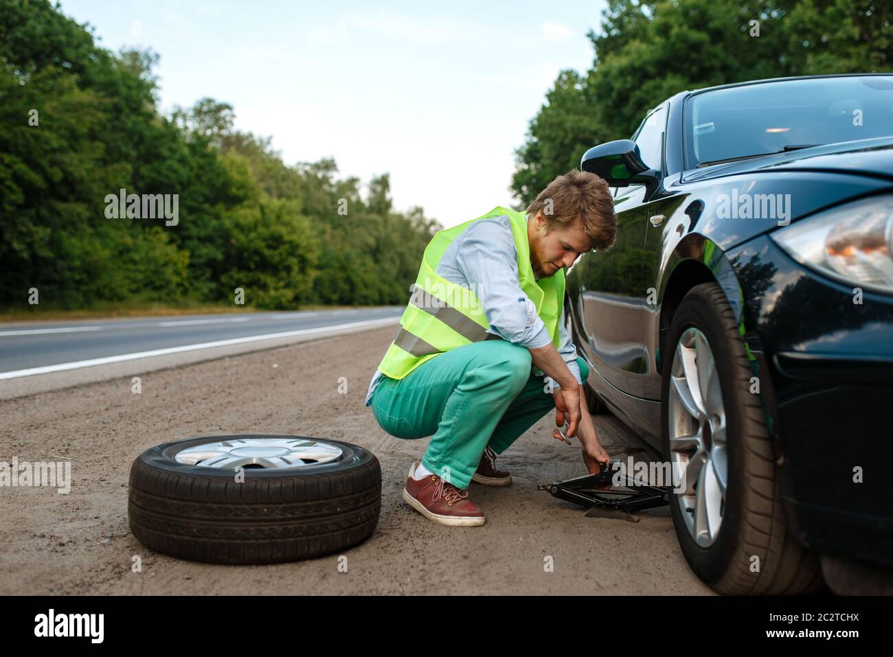 Car breakdown, young man repairing flat tyre. Broken automobile or