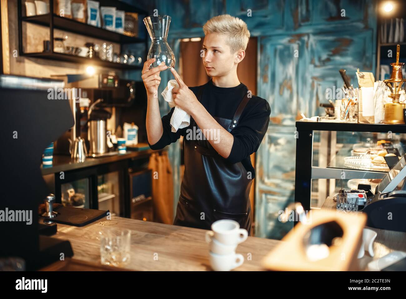Young male barista checks clean dishes after making coffee at cafe ...