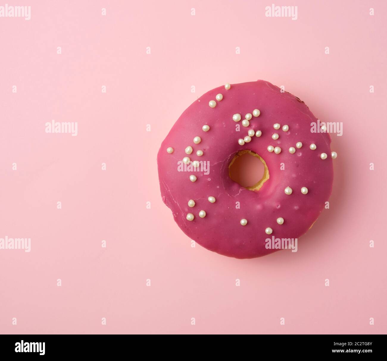 red round donut with white sprinkles on a pink background, top view Stock Photo