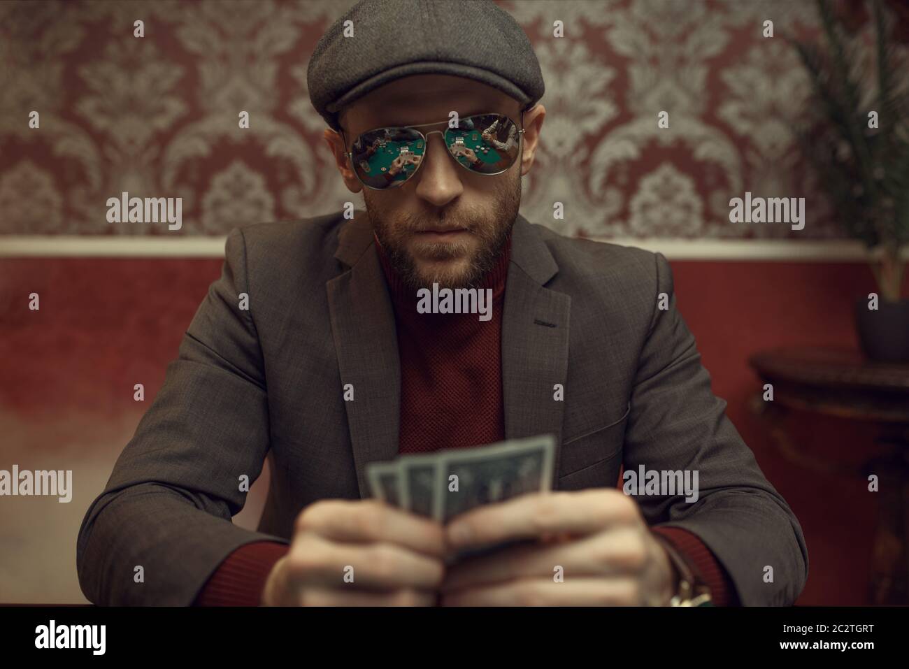 Serious poker player in sunglasses playing in casino. Games of chance addiction. Man with cards in hands leisures in gambling house Stock Photo
