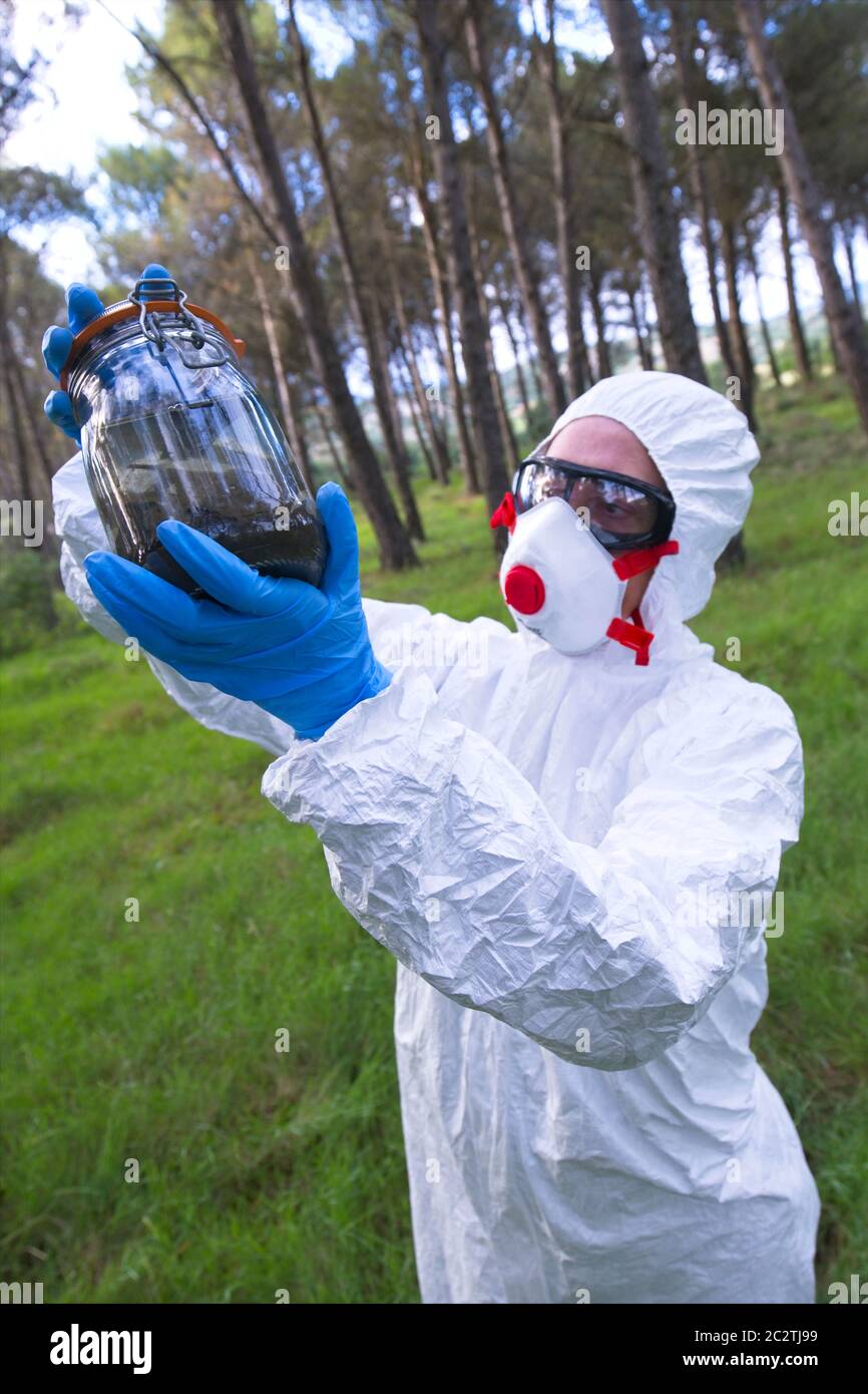 Person with a safety suit with a sample jar in a forest area. Stock Photo