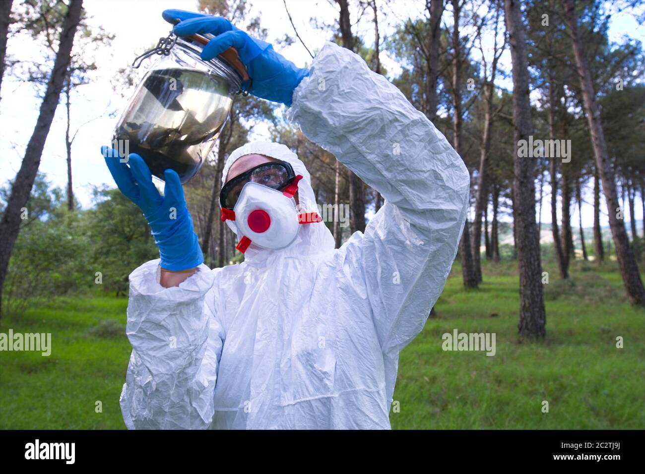 Person with a safety suit with a sample jar in a forest area. Stock Photo