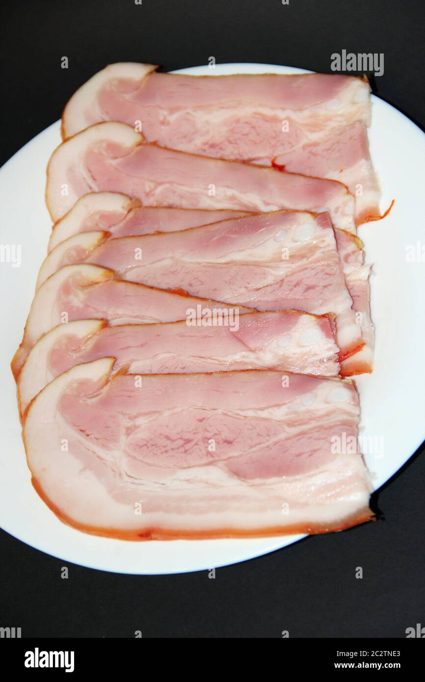 Sliced smoked meat on white plate. Thin slices of sliced bacon. Plate of thin slices of ham Stock Photo