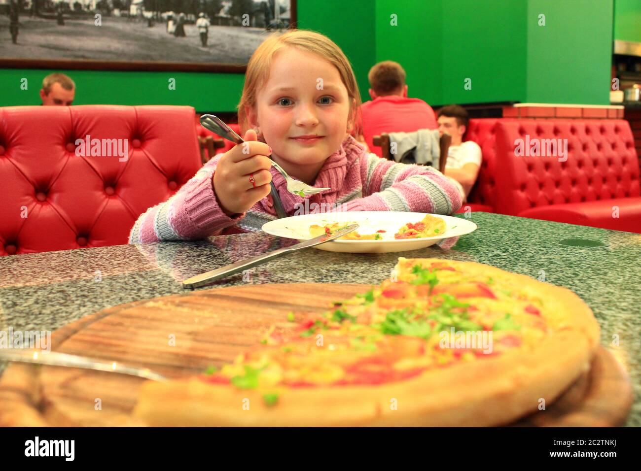 Little girl eating pizza in pizzeria. Big pizza and girl. Delicious fast food meal Stock Photo