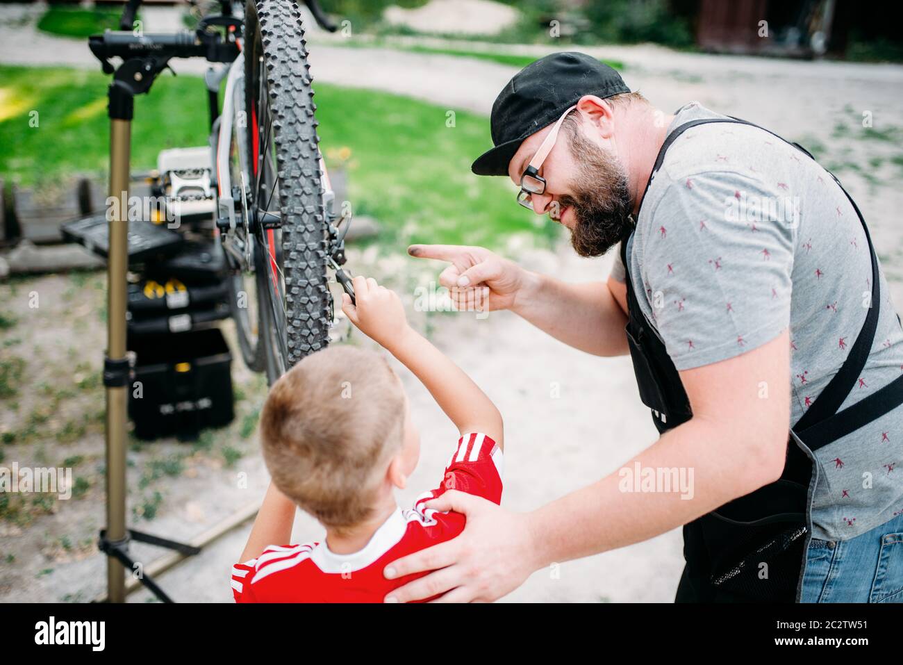 Bicycle mechanic show bike on stand to young boy. Cycle