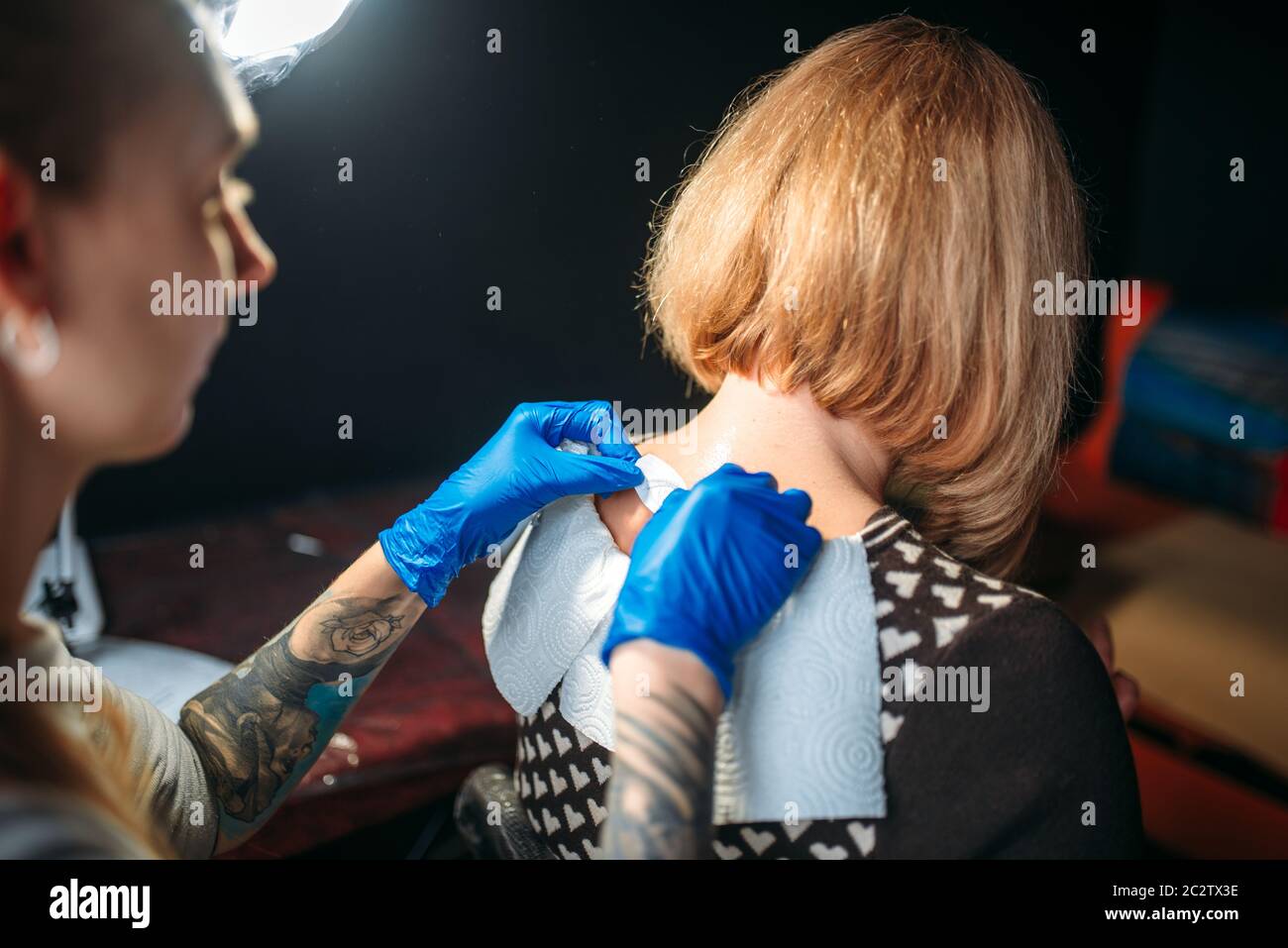 Female tattoo artist in blue sterile gloves prepares client skin for