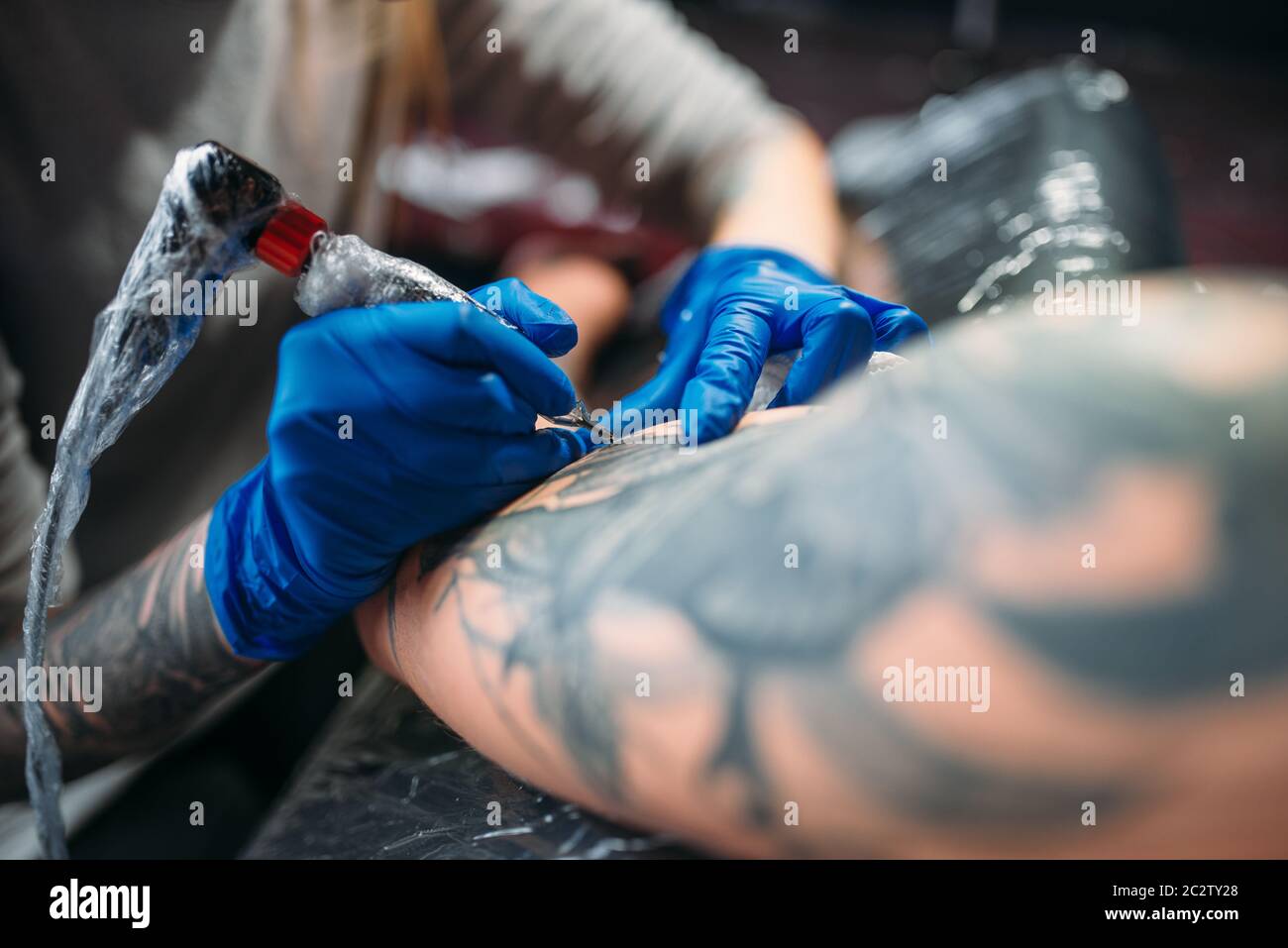 Female tattooist makes tattoo by machine on male shoulder. Professional ...