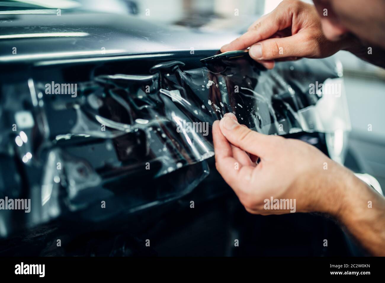 Specialist installs car paint protection film on hood. Transparent