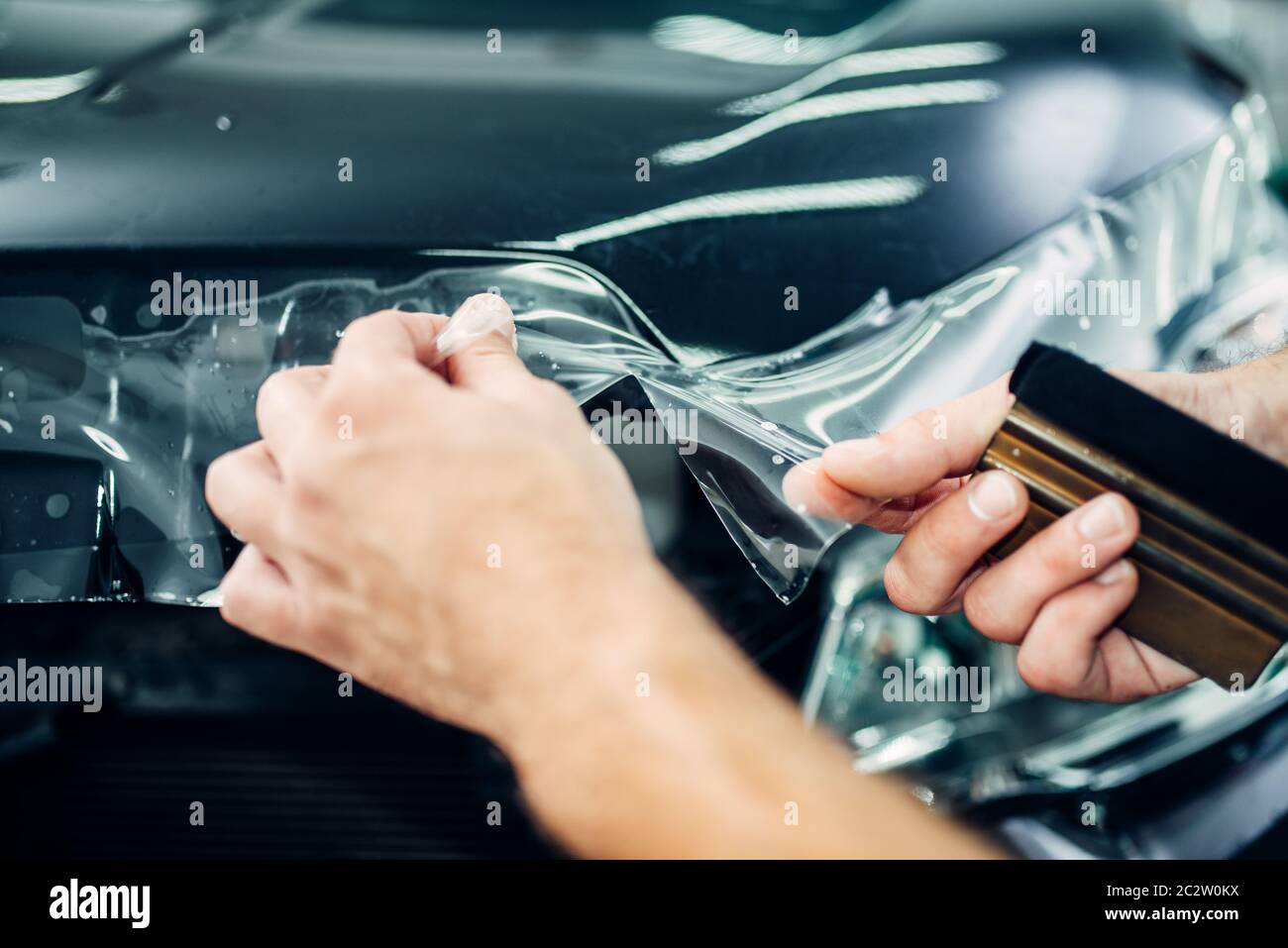 Specialist installs car paint protection film on hood. Transparent