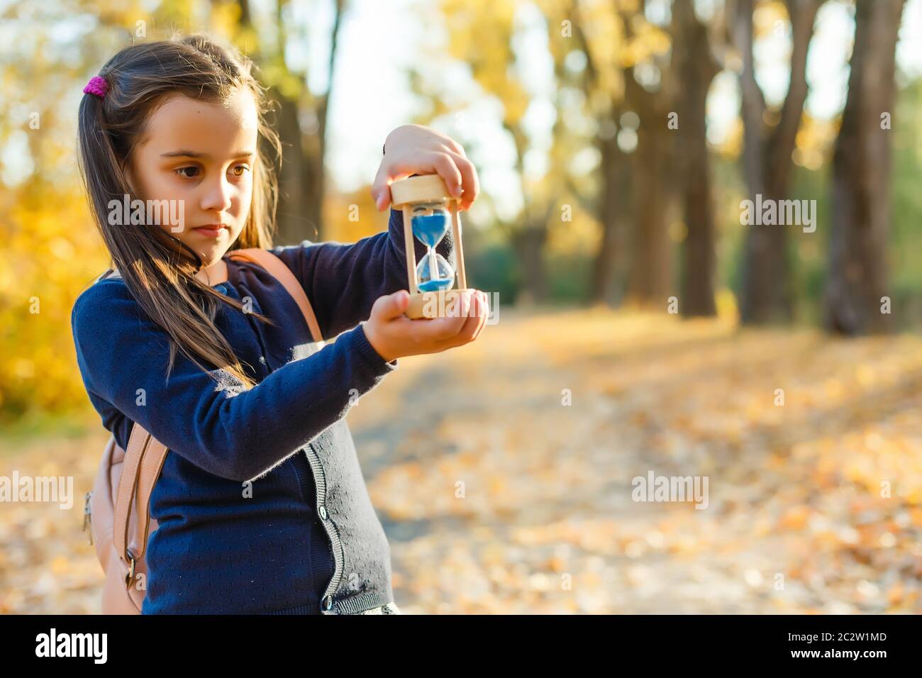 little girl with hourglass surrounded by autumn foliage Stock Photo