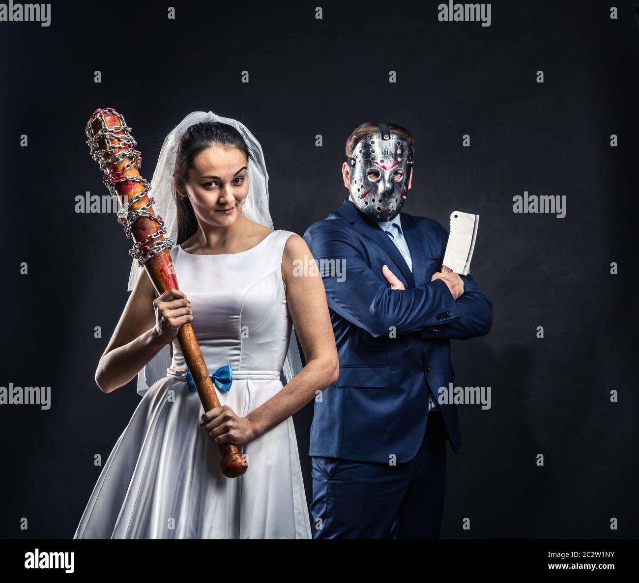Newlyweds serial murderers with bloody bat and meat cleaver, black background. Groom in hockey mask Stock Photo